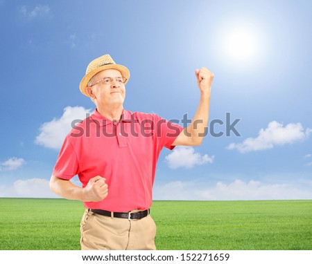 Happy senior man with raised hands gesturing happiness on a field, shot with a tilt and shift lens