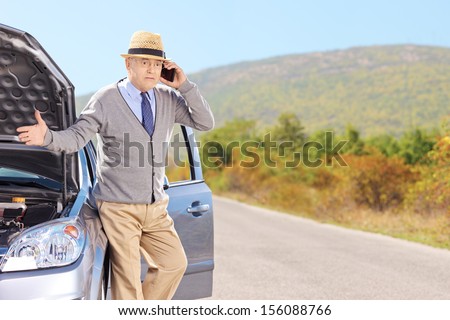 Nervous senior man on a broken car talking on a cell phone