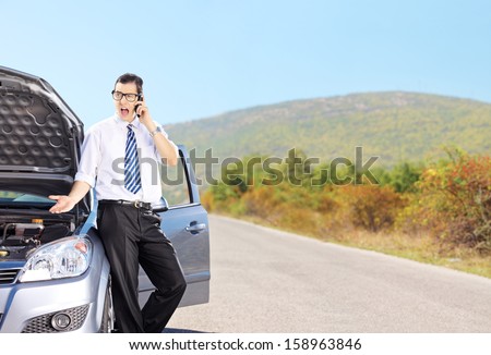 Young nervous male standing next to his broken car and talking on a mobile phone, shot with a tilt and shift lens