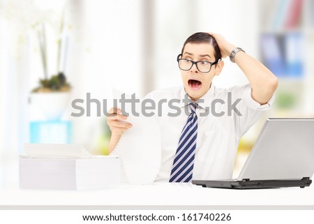 Shocked young accountant in his office looking at very expensive bill