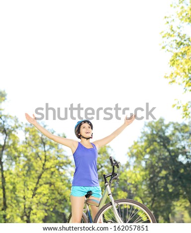 Happy female biker posing with raised hands on a mountain bike outdoors, shot with a tilt and shift