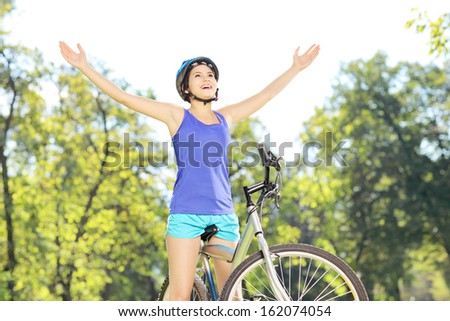 Happy female biker posing with raised hands on a mountain bike outdoors