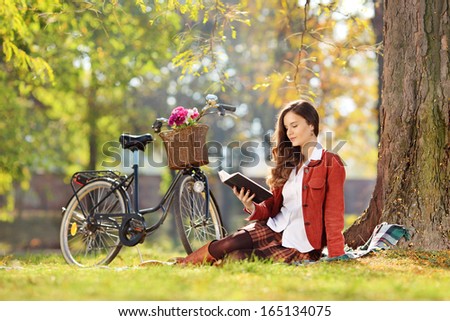 Young pretty woman with a bike reading a novel in a park