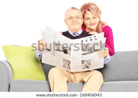 Middle aged couple with newspaper sitting on a couch isolated on white background