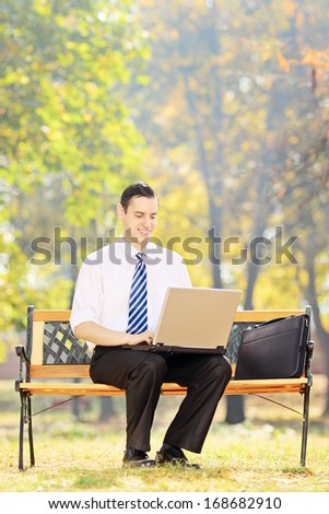 Young businessman sitting on a wooden bench and working on a laptop in a park