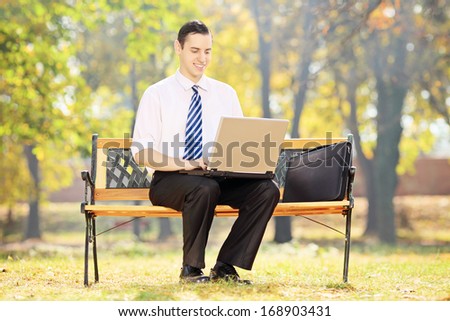 Businessman sitting on a wooden bench and working on a laptop in a park