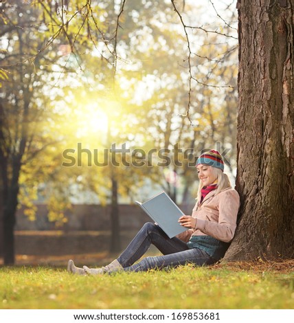 Beautiful girl reading a book and enjoying the sunny day in a park seated on green grass, shot with a tilt and shift lens