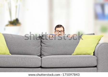 Frightened man hiding behind a sofa isolated on white background