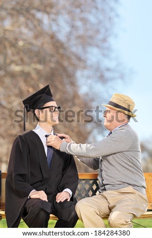 College student and his proud father sitting on wooden bench in park