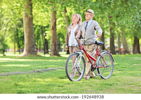 Happy mature couple walking in park and pushing a bike