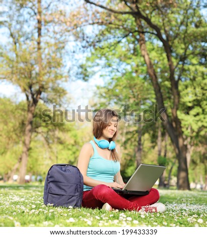 Woman studying with laptop seated on grass in park shot with tilt and shift lens