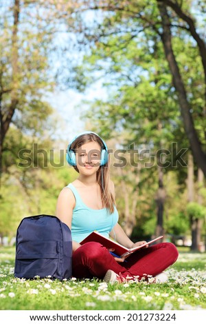 Young girl with headphones studying in park seated on grass
