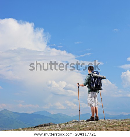 Male hiker standing on a mountain top and holding hiking poles shot with tilt and shift lens