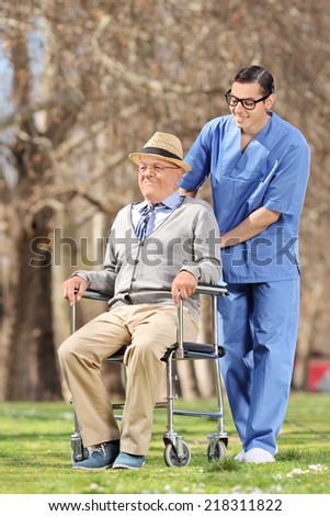 Male nurse pushing a senior in wheelchair outdoor on a sunny day