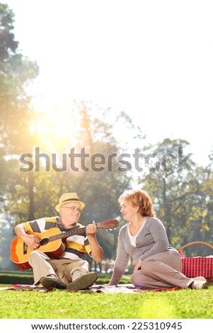 Vertical shot of a senior playing guitar to his wife in a park