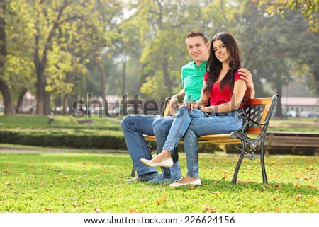 Young couple posing seated on a bench in park on a sunny day