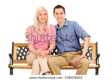 Cheerful young couple posing seated on a bench isolated on white background