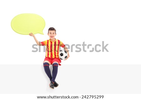 Junior football player holding a speech bubble seated on a panel isolated on white background