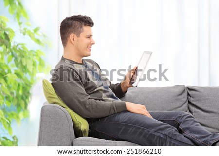 Young guy reading something on a tablet seated on a sofa at home