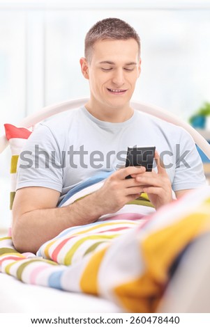 Young man texting someone from his cell phone and lying in bed isolated on white background