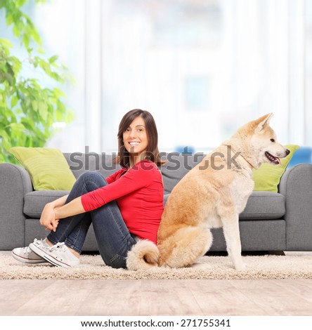 Young woman posing seated beck to back with her pet dog in front of a modern gray sofa at home shot with tilt and shift lens