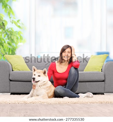 Young woman relaxing at home seated on the floor with her pet dog in front of a modern sofa shot with tilt and shift lens