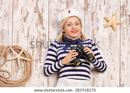 Female sailor lying on a deck with binoculars in her hand and looking at the camera