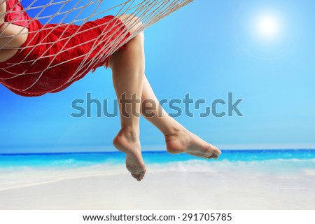 Close-up on the legs of a woman lying in a hammock on a beach by the open sea
