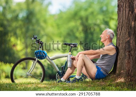 Active senior man listening to music on headphones seated by a tree in a park