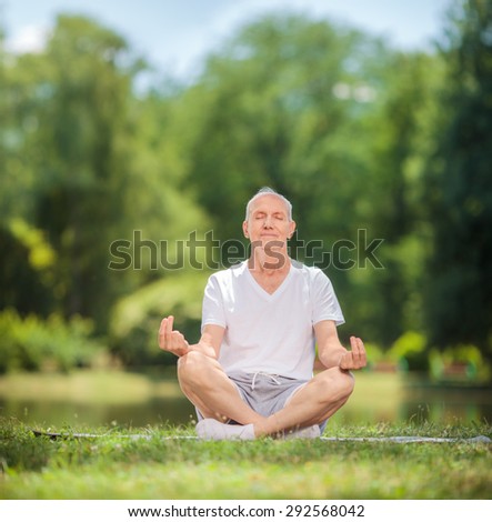 Peaceful senior man meditating seated on a blanket in a park by a lake shot with tilt and shift lens