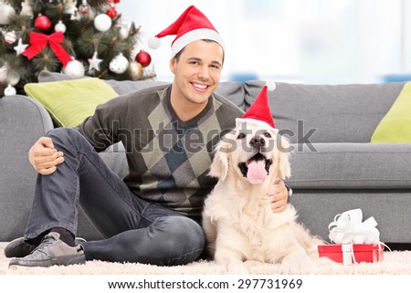 Man and a dog with Santa hats sitting by a sofa at home