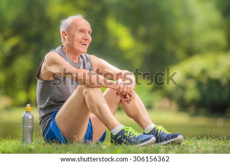 Athletic senior in sportswear sitting on grass in a park and listening to music on headphones