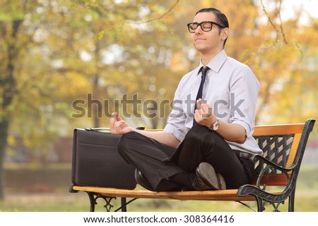 Relaxed young businessman meditating seated on a bench in park