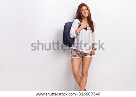Teenage schoolgirl posing with a blue backpack and leaning against a wall
