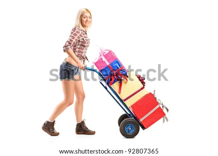 Full length portrait of a female manual worker pushing a handtruck with presents on it isolated on white background