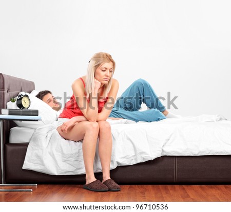 Upset woman sitting on a bed while her boyfriend is sleeping with the camera focus on her