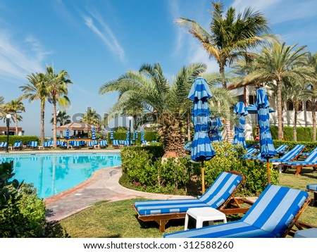 DUBAI, UNITED ARAB EMIRATES (UAE) - JAN 28, 2014: Sunbeds, palm trees and pool in tropical garden of luxury hotel beach resort