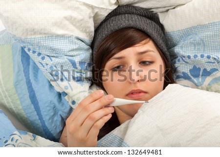 The young girl is lying sick in bed and taking her temperature