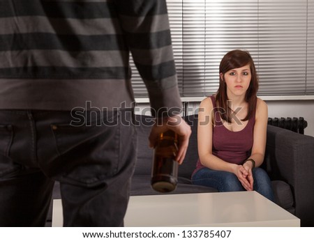 The man is standing with a bottle of beer in front of his girlfriend