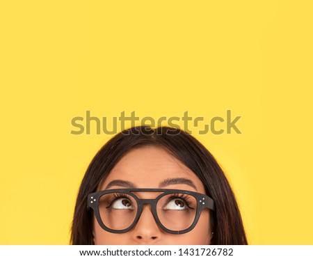 closeup portrait headshot cropped face above lips of cute happy woman in glasses looking up isolated on yellow studio wall background with copy space above head. Human face expressions, emotions Foto d'archivio © 