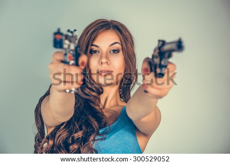 Beautiful  young woman, girl with 2 guns isolated on green wall. Brunette holding Handguns looking, aimed, pointing at you camera. Portrait close up. Violent rebel gangster bandit self justice concept