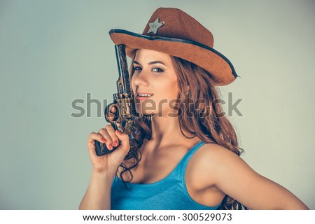 Beautiful  young woman, girl with gun isolated on green wall. Brunette holding Handgun arm supports lift up her sheriff on head. Portrait close up. Violent rebel gangster bandit self justice concept.