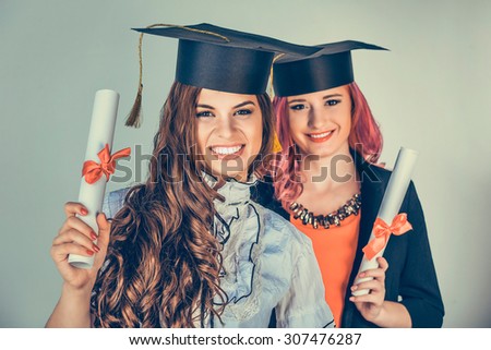 Portrait closeup beautiful happy  graduates, two graduated student girls, young women in cap gown turning smiling holding diploma scroll isolated green background wall. Celebrating graduation ceremony