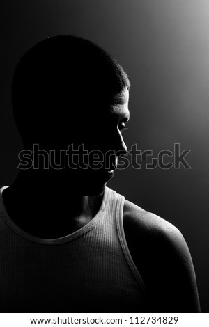 Silhouette of a man\'s face, on a profile view with dark background and back lighting. The guy has muscles is looking to the side.