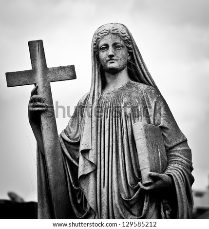Statue of Mary with a bible and a cross on the cemetery, with creepy look.