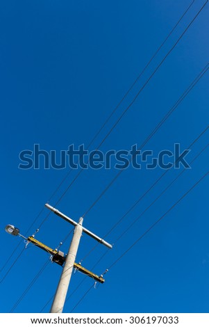 Power pole and power lines with a street light on blue sky.