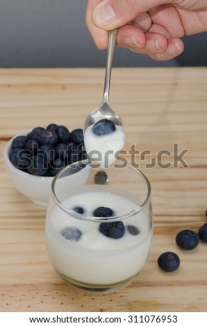 Hand holding a spoon on yogurt with blueberries over wood table