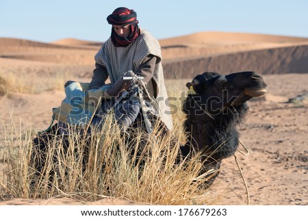 ERG CHEBBI, MOROCCO - JANUARY 06: An unidentified Bedouin with camel waiting for tourist on January 06, 2014 in Western Sahara, Morocco. Tourism is an important item in the economy of Morocco