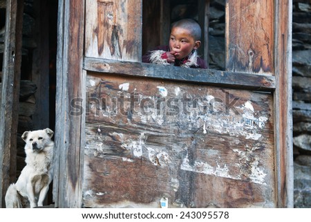 LHO, MANASLU CONSERVATION AREA, NEPAL - NOVEMBER 29: Unidentified Tibetan boy Lapsang, 9, with white dog poses for a photo at him home on November 29, 2009 in Lho village, Tsum valley, Nepal