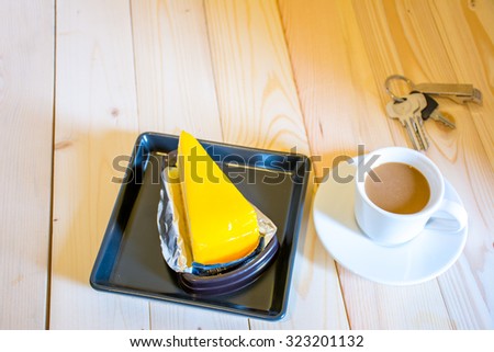 Coffee cup with orange cake in the morning sunshine on wood floor.
